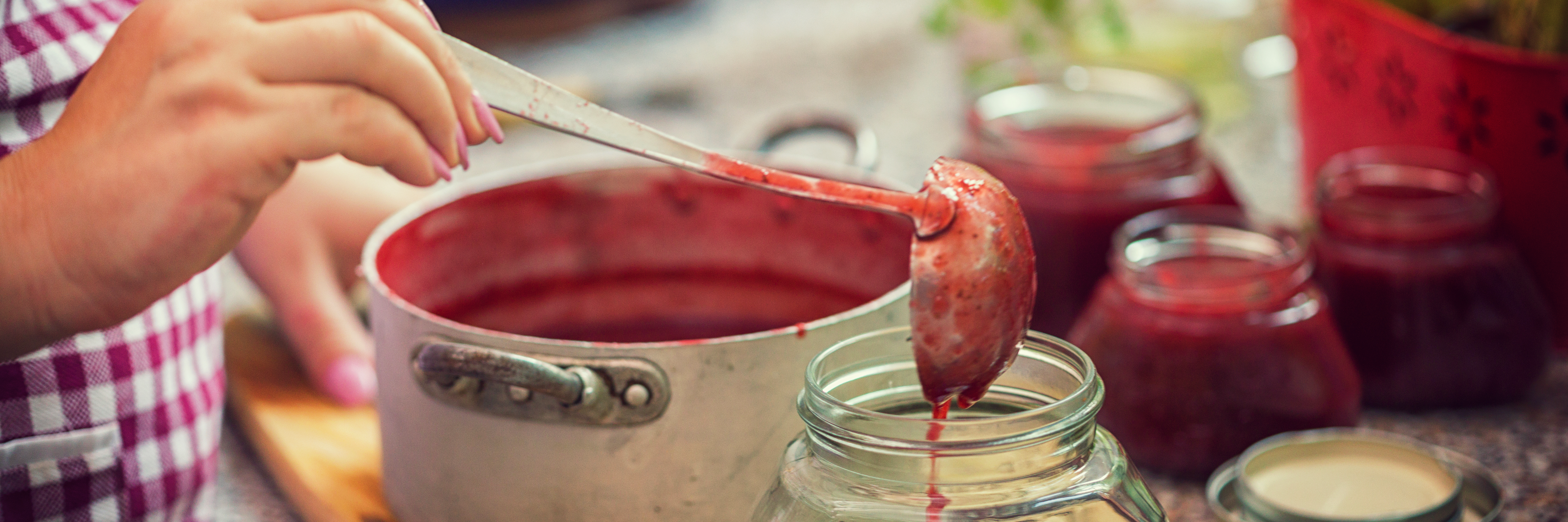 Frau füllt rote Marmelade in ein Marmeladenglas
