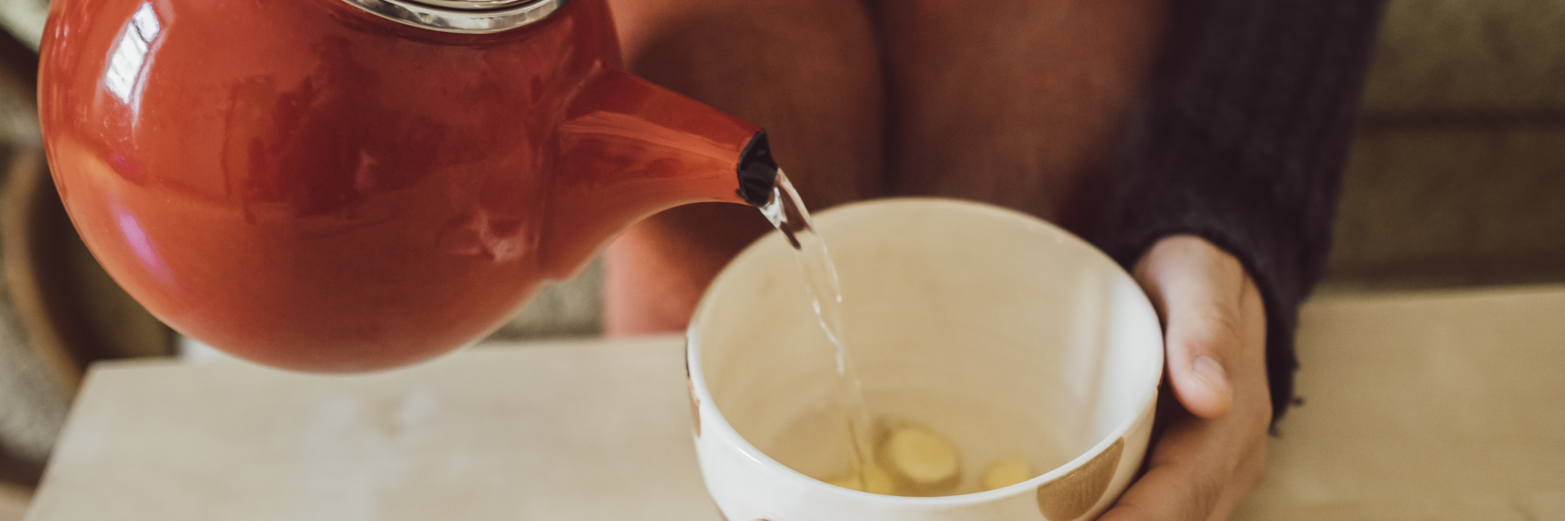 Frau schenkt Tee aus roter Kanne in eine Teetasse